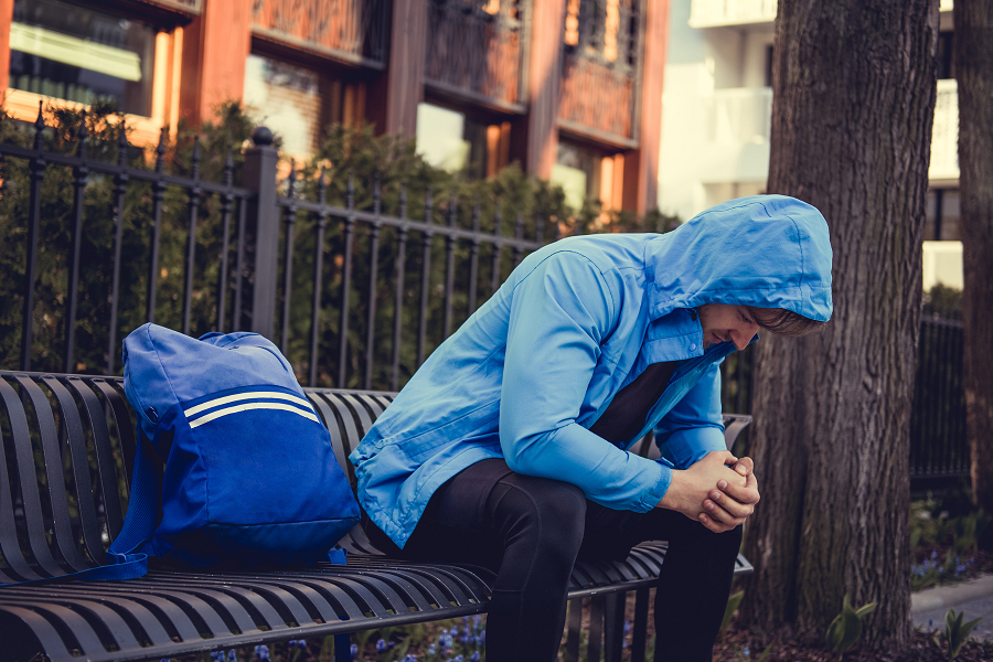 person sitting n a bench wearing a blue jacket, hunched over and in distress