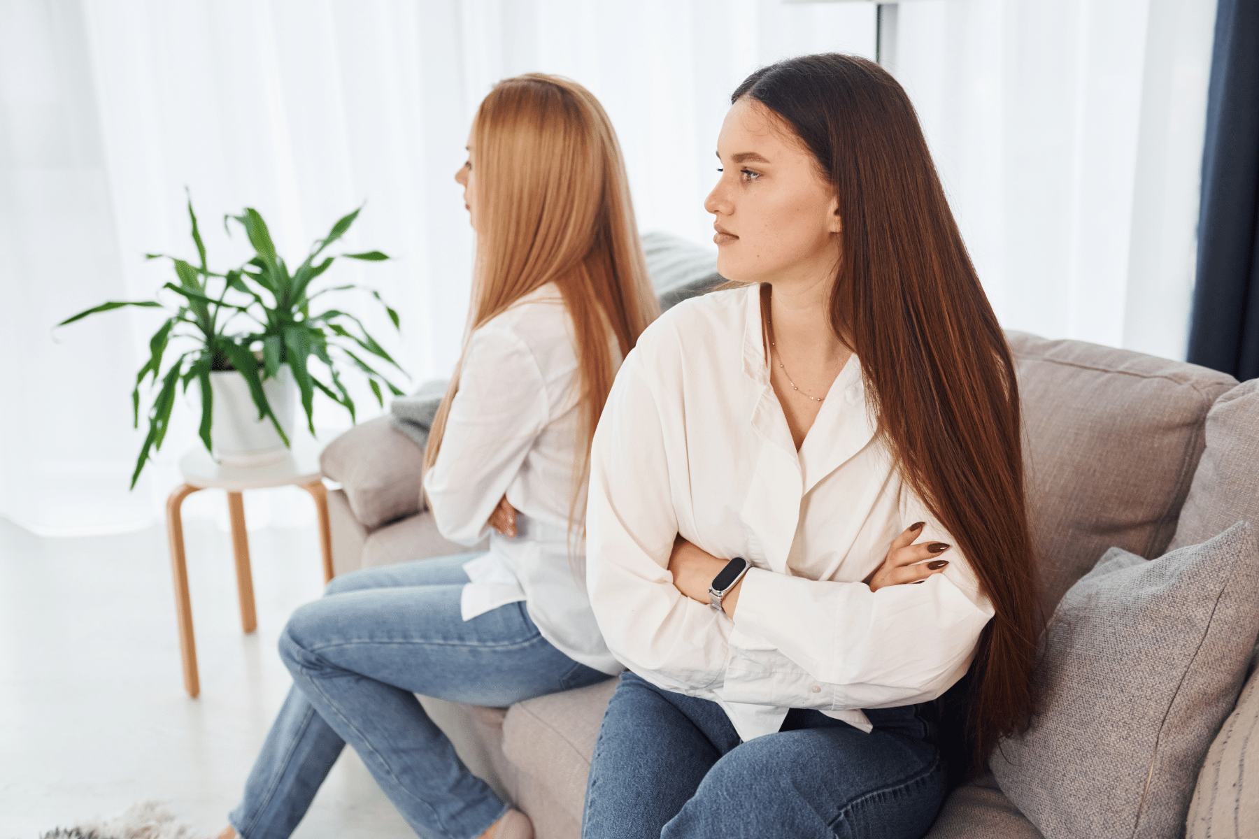 picture of two women sitting on either end of a couch both looking away with their arms crossed