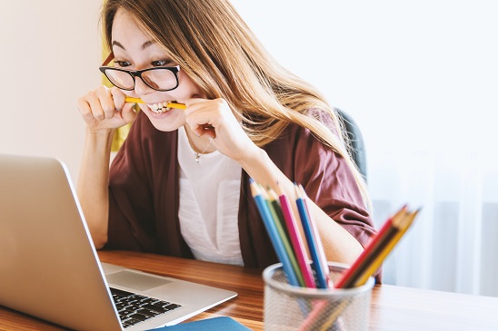 Young woman sitting at her laptop, stressed and biting her pencil